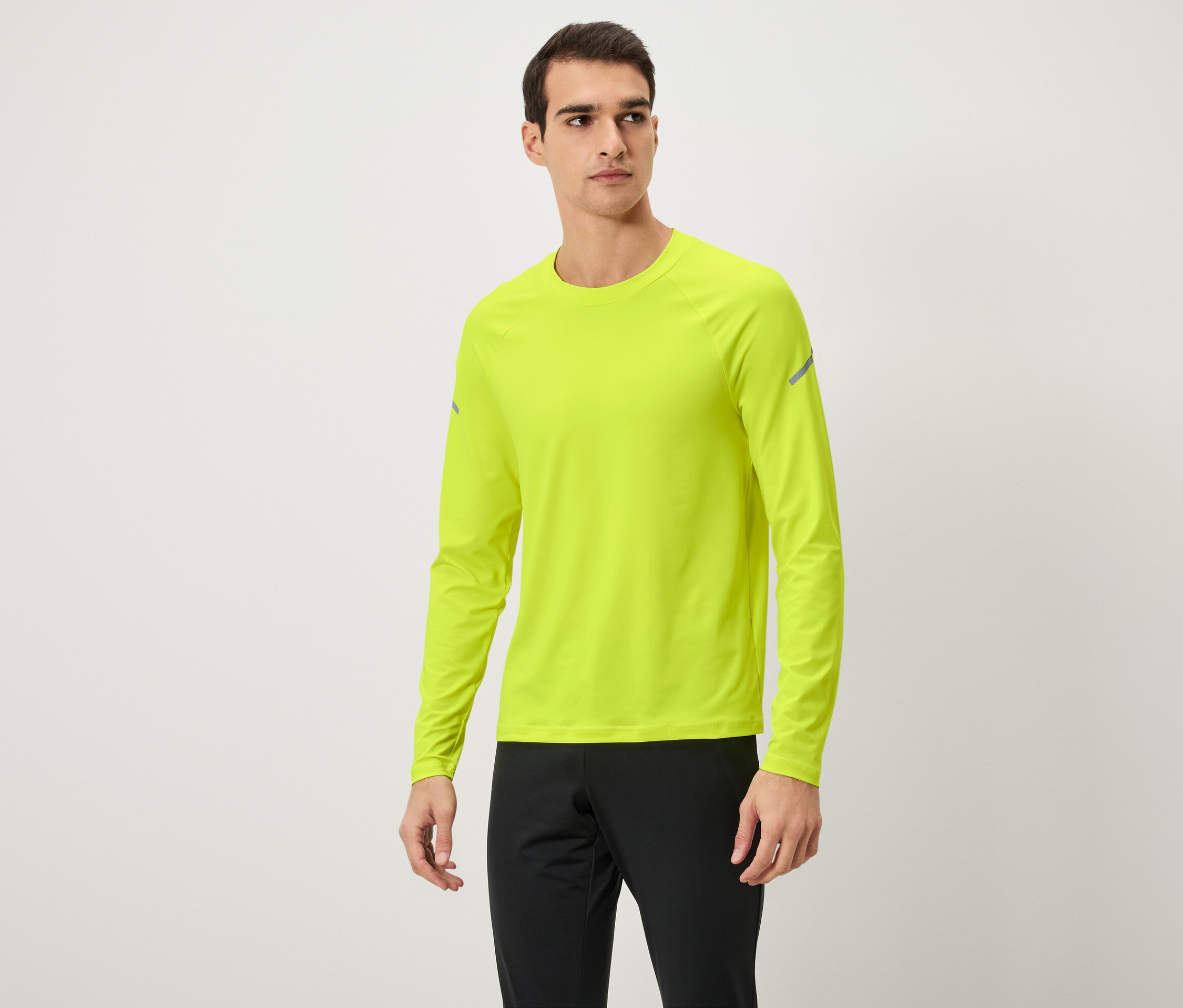 Mężczyzna pozuje w neonowożółtej koszulce z długim rękawem i czarnych spodniach dresowych.