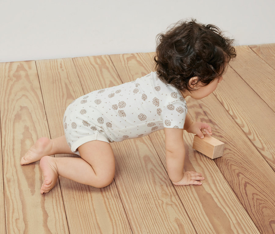 Raczkujący na drewnianej podłodze niemowlak w białym body z krótkim rękawem, 5 sztuk.