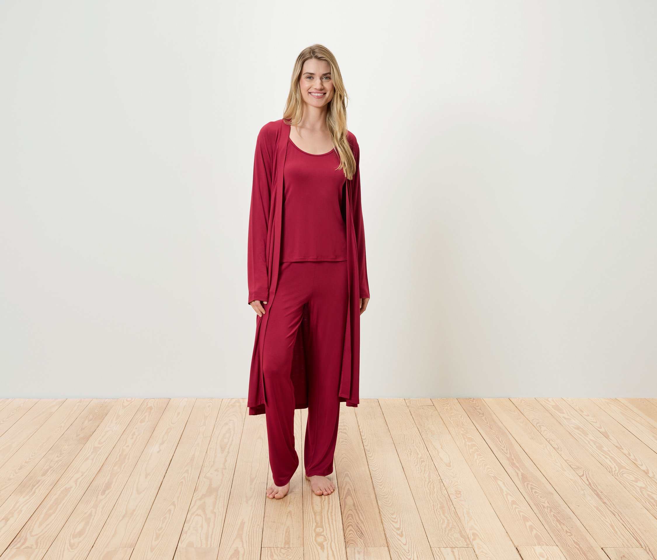 Kobieta stoi w bordowej piżamie składającej się z podkoszulka, spodni i szlafroka.