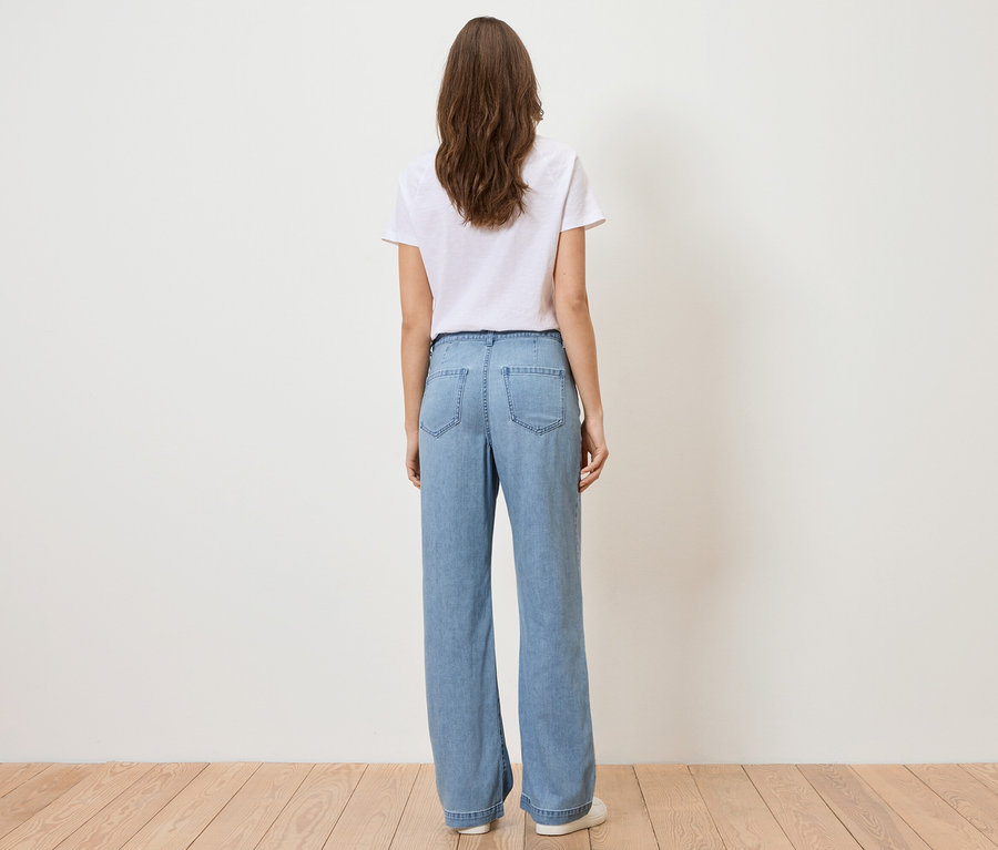 Widok z tyłu kobiety z długimi brązowymi włosami, ubranej w biały T-shirt i jasnoniebieskie dżinsy.