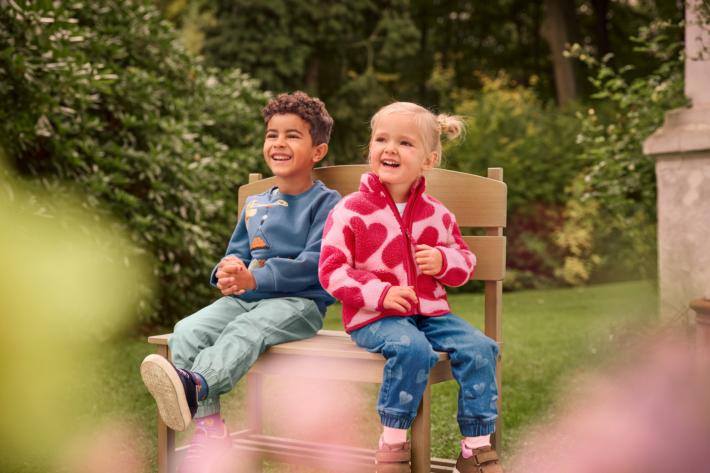 Chłopiec i dziewczynka siedzą i śmieją się na małej ławce ogrodowej z półką.