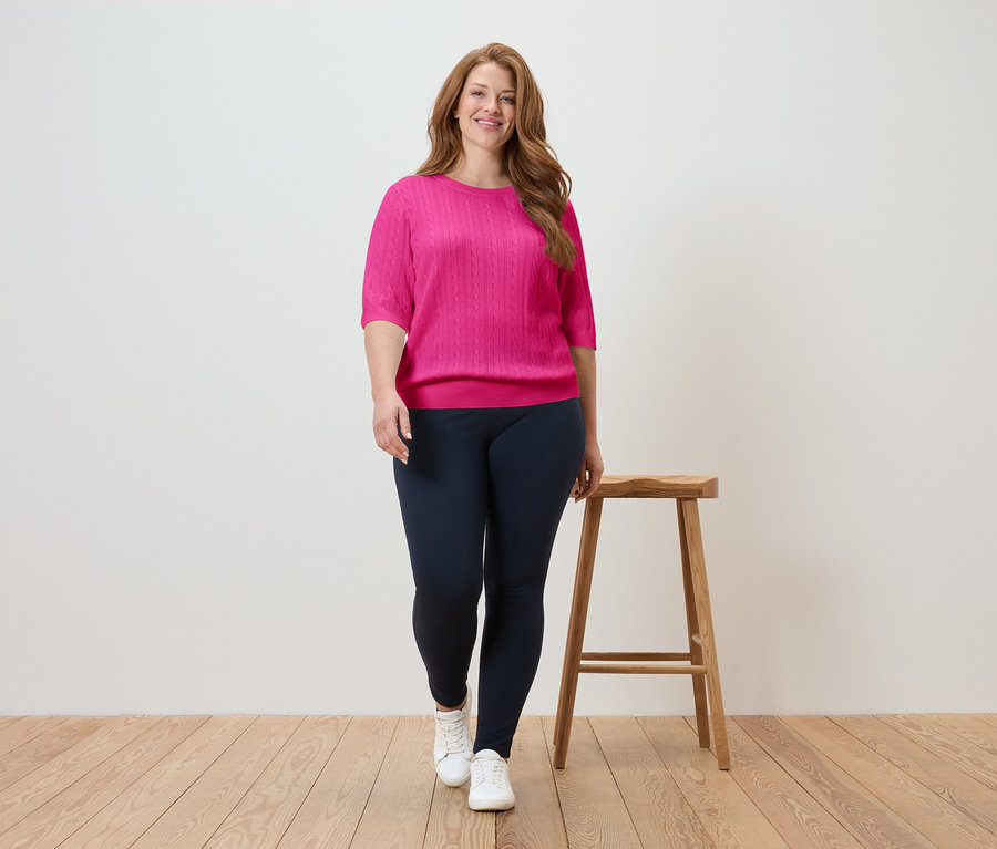 Kobieta idzie w różowym topie i granatowych legginsach na drewnianej podłodze