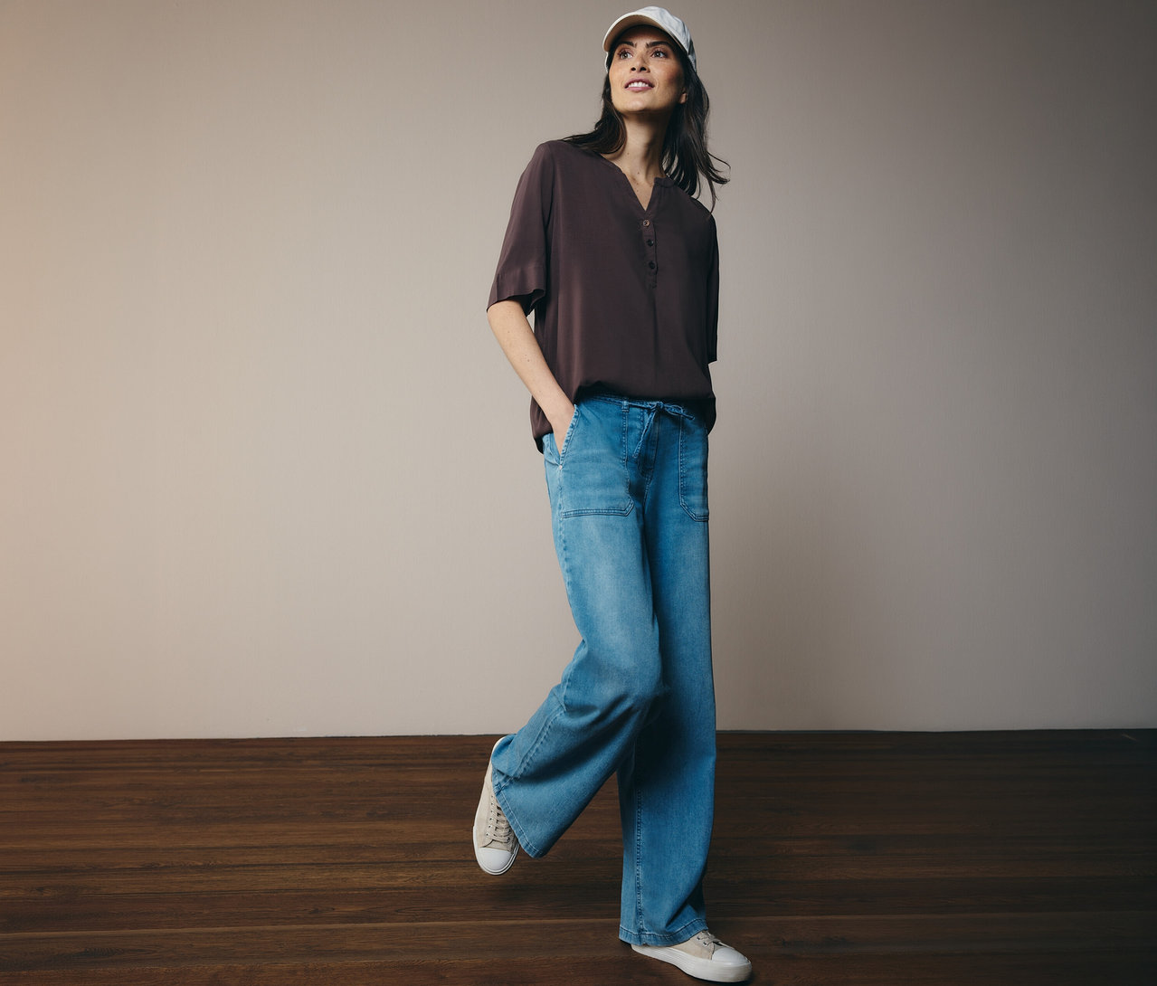 Kobieta w czapce z daszkiem i brązowej bluzce tunikowej CECIL, dżinsach i trampkach.