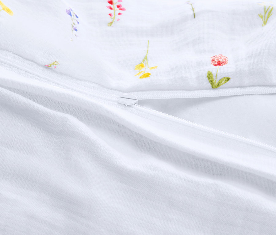 Szczegółowy widok częściowo otwartego, białego śpiwora z zamkiem błyskawicznym i kwiatowym wzorem.