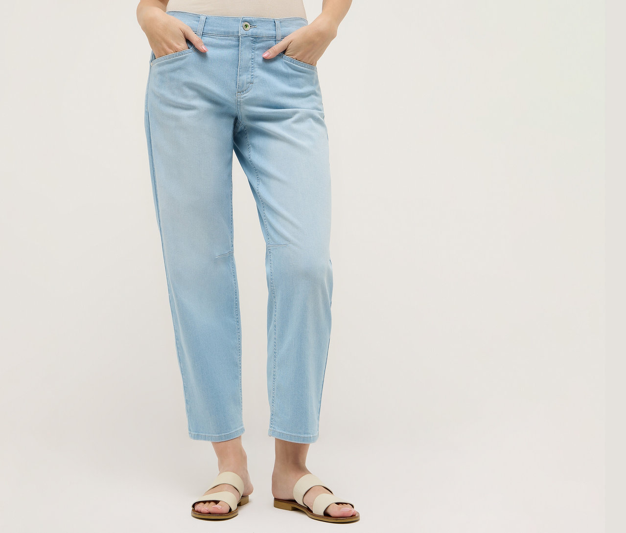 Kobieta w jasnoniebieskich jeansach Angels „Evy Cool” O-Shape i sandałach. Ręce ma w kieszeniach.
