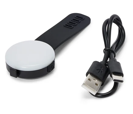 Na białym tle leży czarne, okrągłe światło LED z czarnym uchwytem i kablem USB.