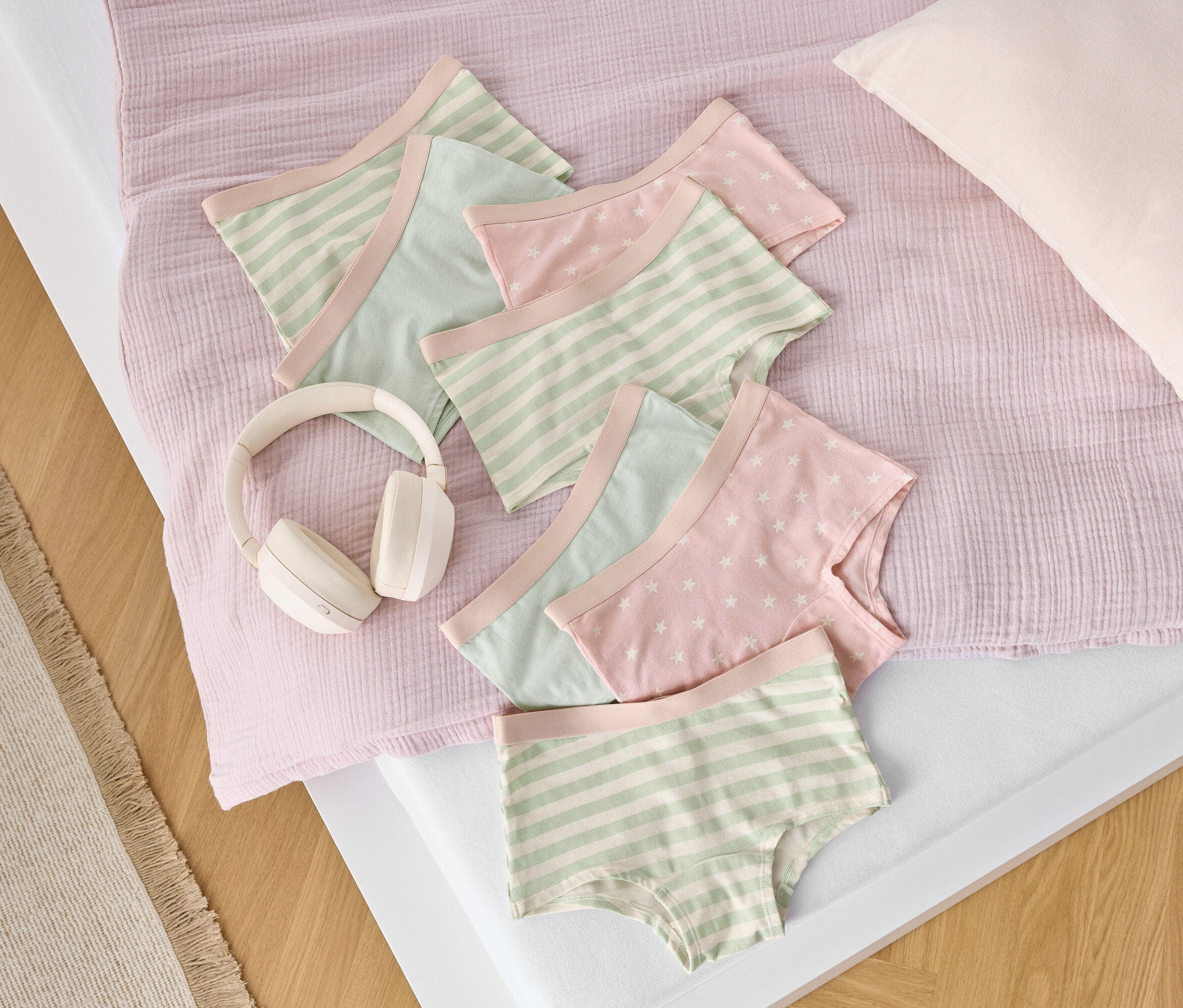 Na łóżku leżą bawełniane majtki w paski i gwiazdki obok białych słuchawek.