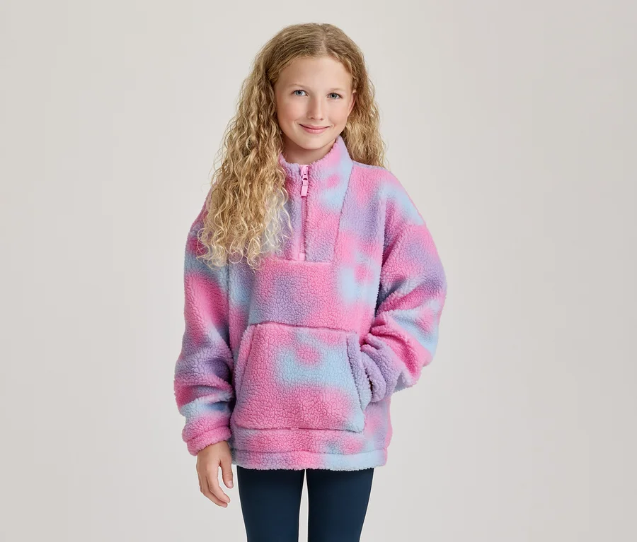 Uśmiechnięta dziewczynka z kręconymi blond włosami w różowo-fioletowo-niebieskim polarowym pulowerze tie-dye z zamkiem i kieszenią.