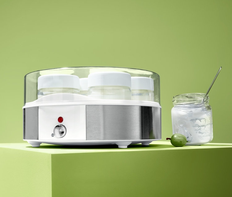 Elektryczna jogurtownica z siedmioma słoikami stoi obok słoika jogurtu i zielonego agrestu.