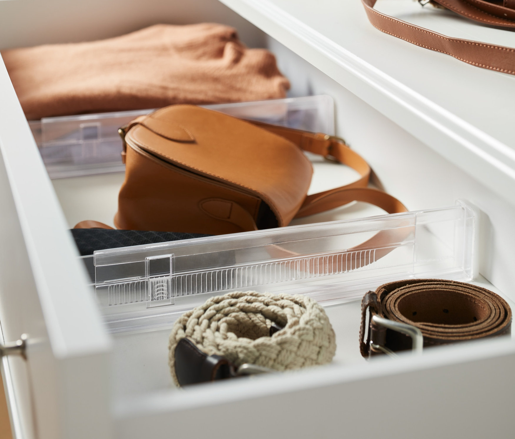 Otwarta szuflada z 2 przegrodami, swetrem, torebką i paskami.