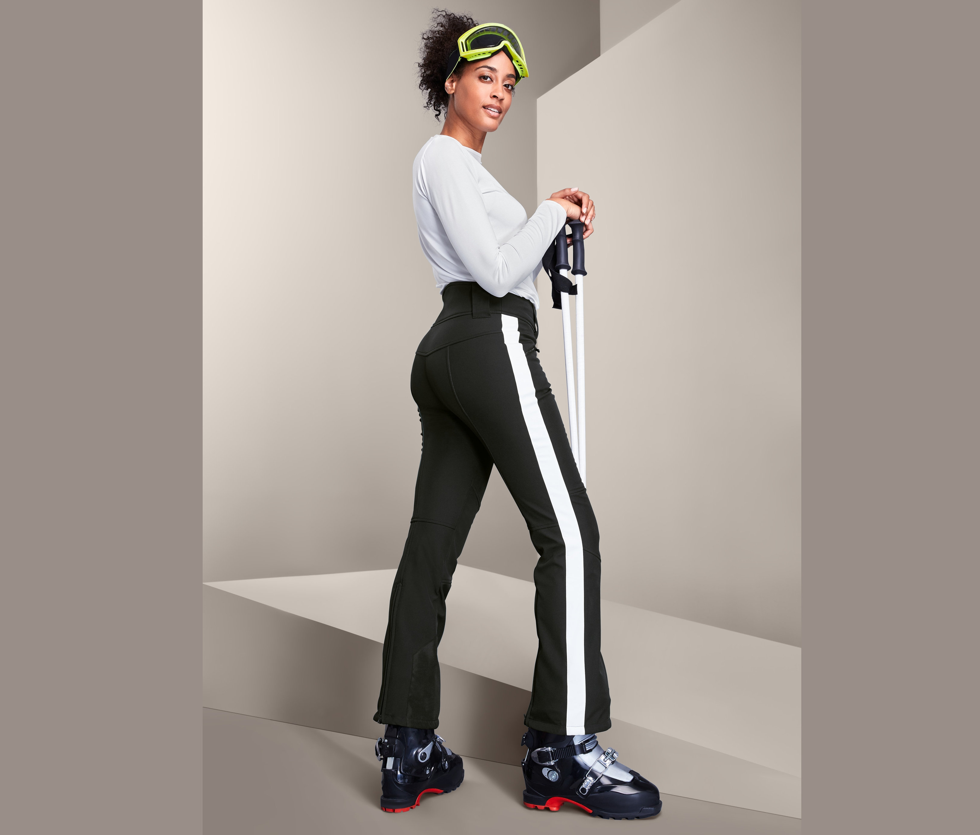 Kobieta w butach narciarskich trzyma kije narciarskie i ma na sobie damskie spodnie narciarskie Jet Ski.