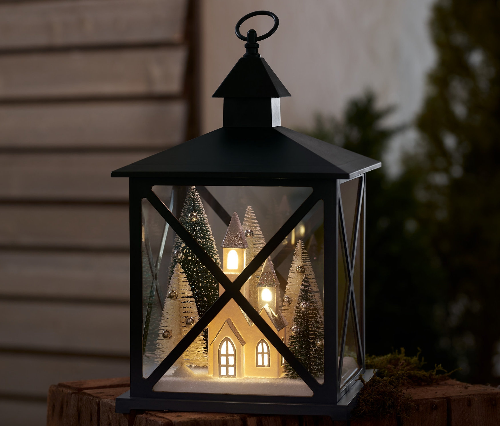 Latarnia dekoracyjna LED z motywem zimowego lasu stoi na drewnianej powierzchni.