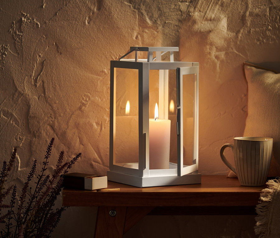 Lampion ze świecą stoi na drewnianym stole obok kubka i kwiatu.