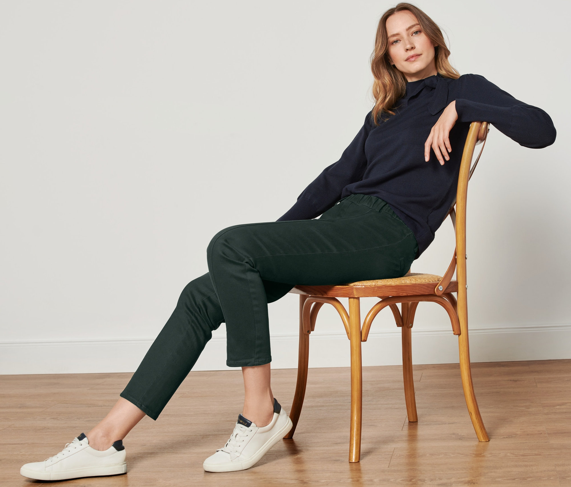 Kobieta siedzi na krześle i ma na sobie ciemnozielone spodnie z tkaniny twill z wygodnym wykończeniem w pasie.