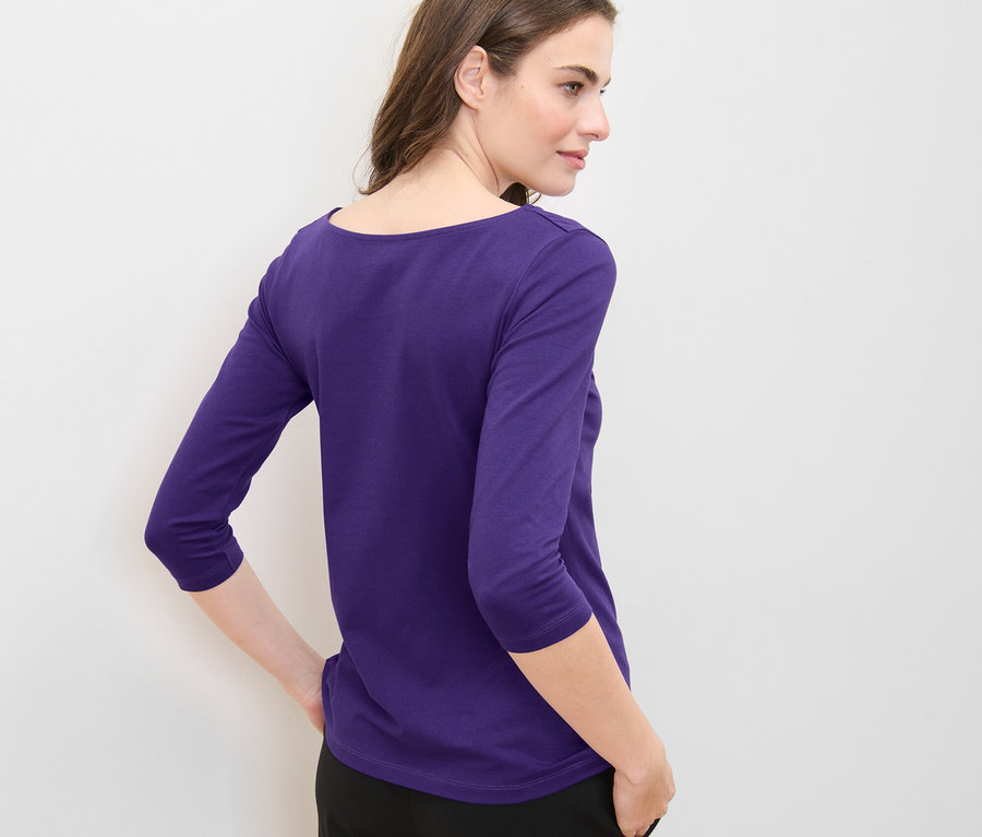 Kobieta pozuje w fioletowej koszulce z rękawami o długości 3/4.