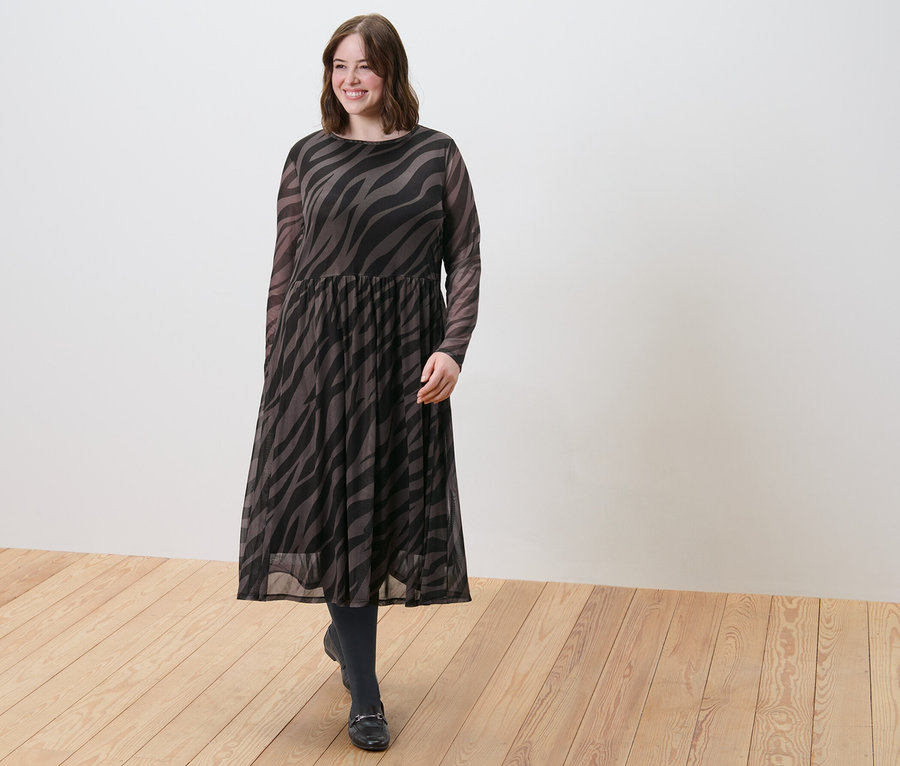 Kobieta idzie po drewnianej podłodze w sukience midi i cienkich rajstopach, 2 pary, 80 den, czarne.