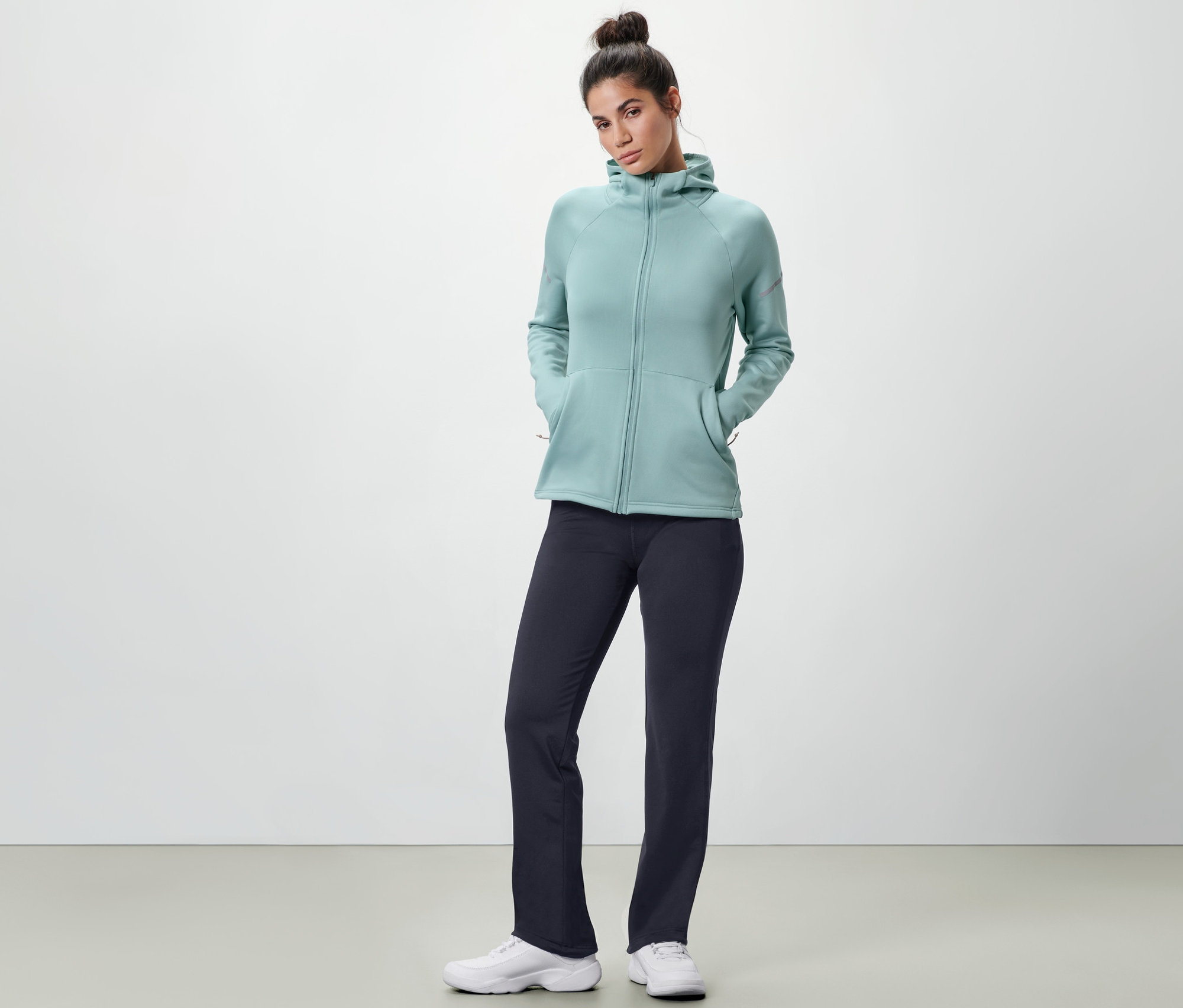 Kobieta pozuje w granatowych spodniach termoaktywnych i jasnoniebieskiej bluzie z kapturem.