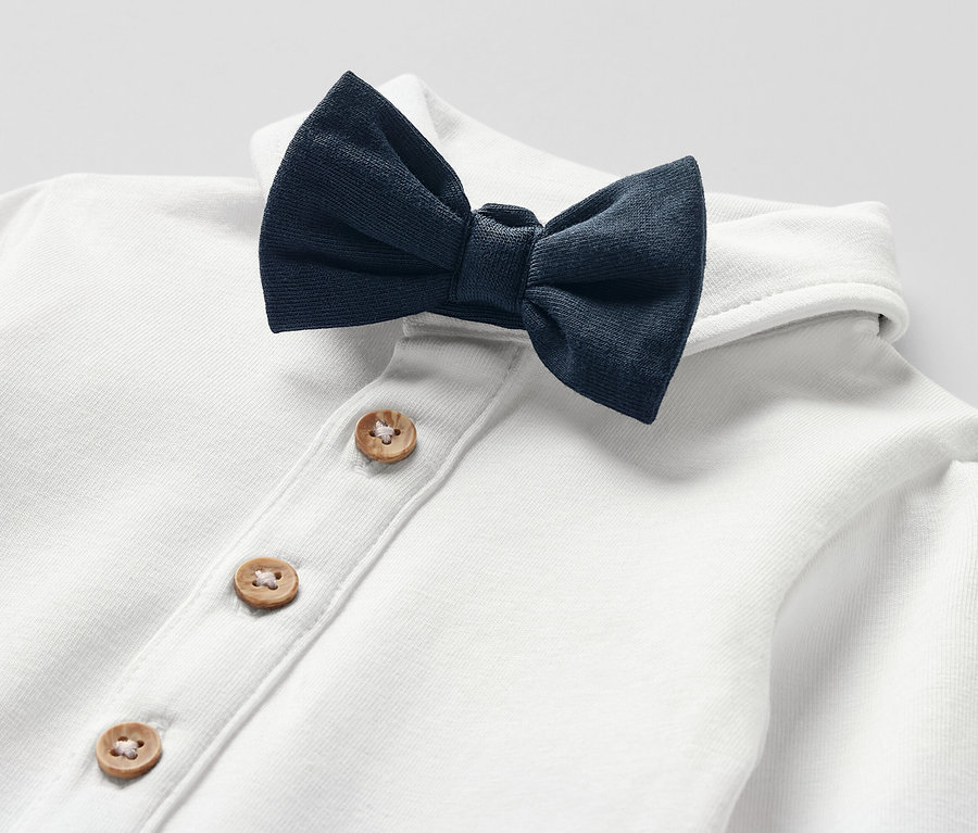 Zbliżenie na białe body z muchą dla niemowląt, zapinane na drewniane guziki.