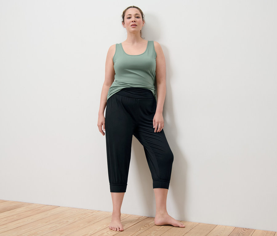 Kobieta pozuje w zielonym topie i czarnych spodniach do jogi o długości 3/4.