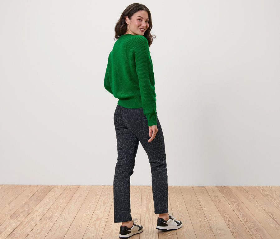 Kobieta patrzy przez ramię, ubrana w zielony sweter i spodnie dżinsowe – fason „Kira”.