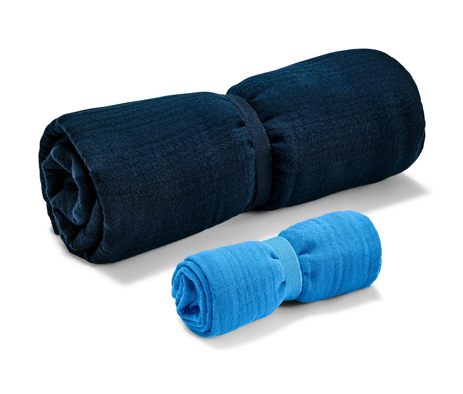 Dwa muślinowe ręczniki podróżne zwinięte i związane gumką.