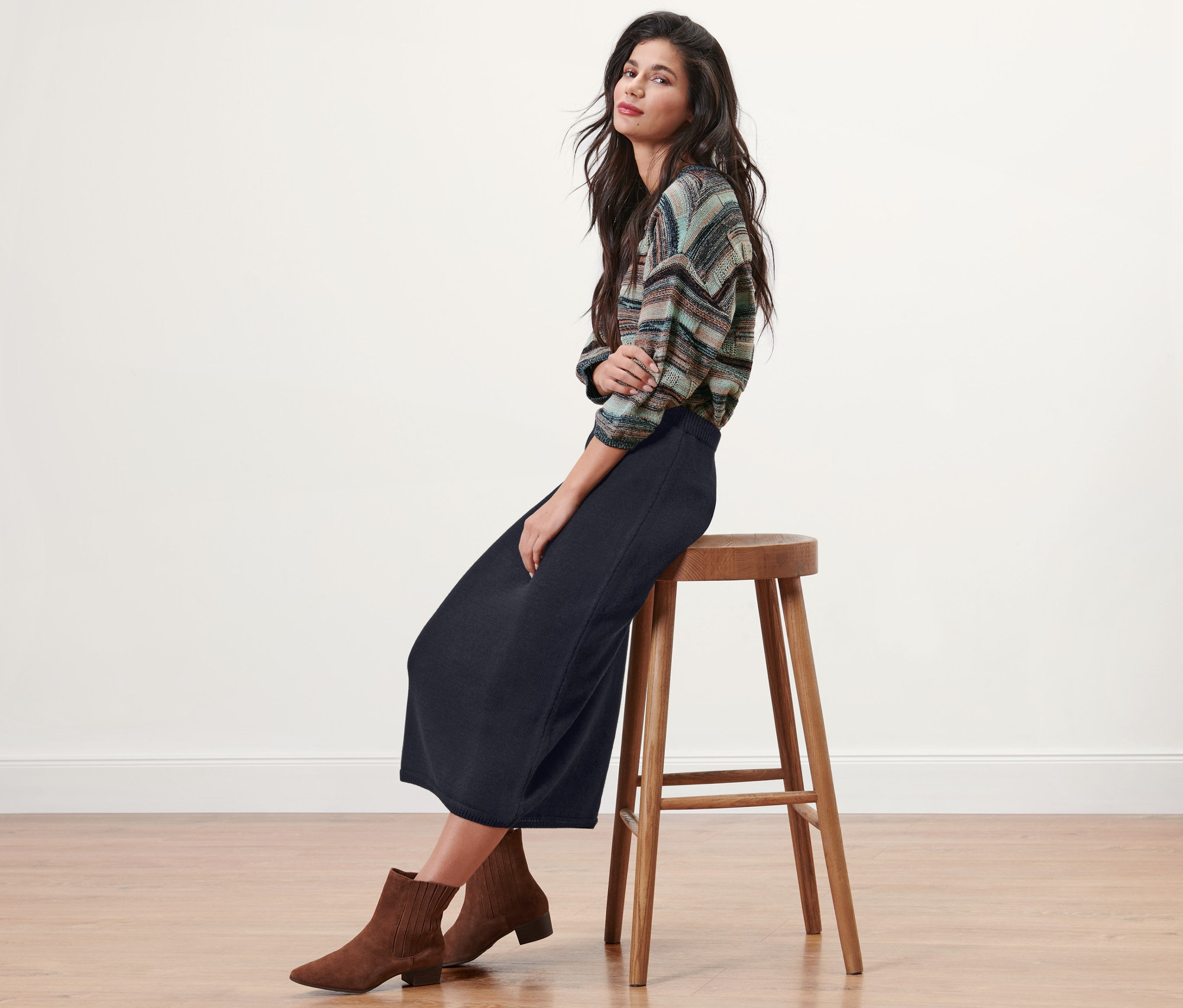 Brunetka siedzi na stołku, ubrana w granatową spódnicę z dzianiny.