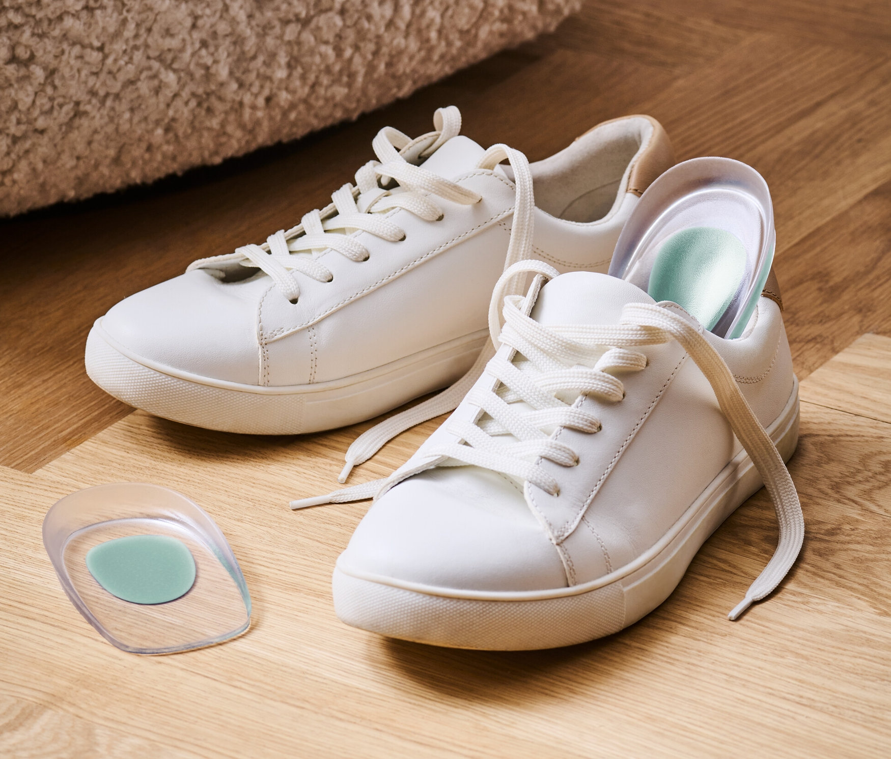 Dwa białe tenisówki i 1 para podpiętek na drewnianej podłodze.