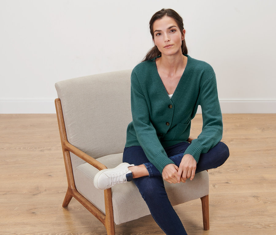 Kobieta siedzi w fotelu i ma na sobie ciemnozielony rozpinany sweter z zawartością wełny.