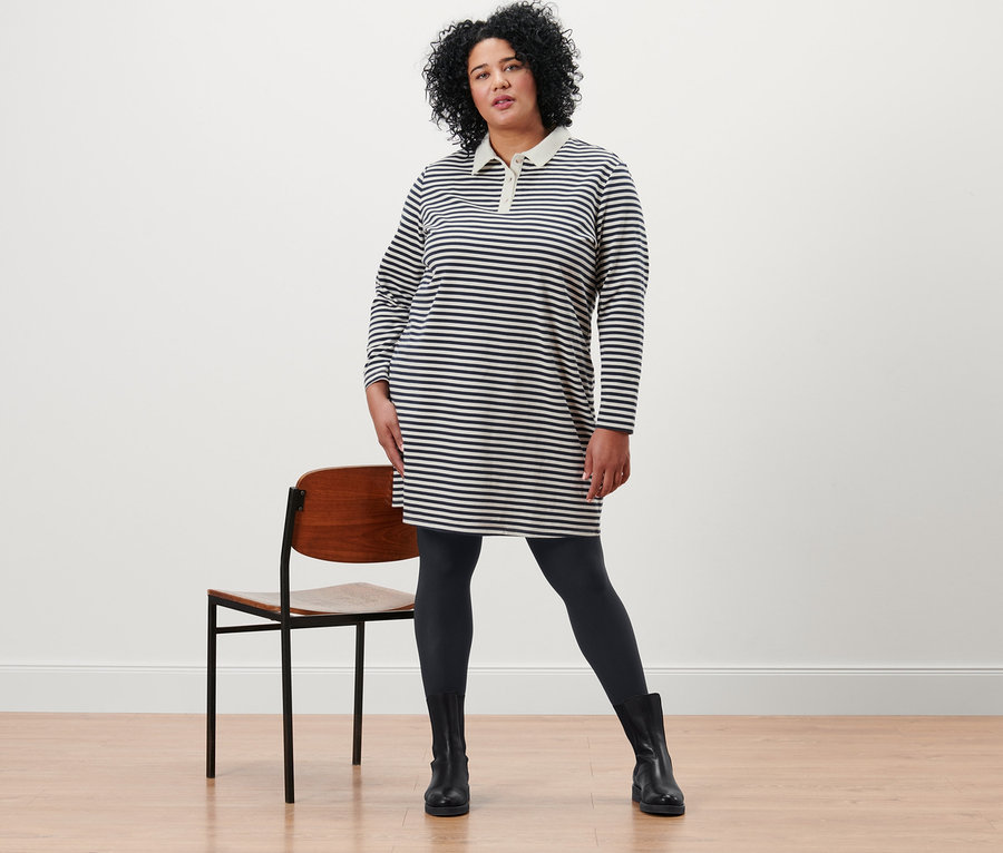 Kobieta pozuje w sukience z dzianiny dresowej z kołnierzykiem polo i kryjących rajstopach (2 pary, czarne).