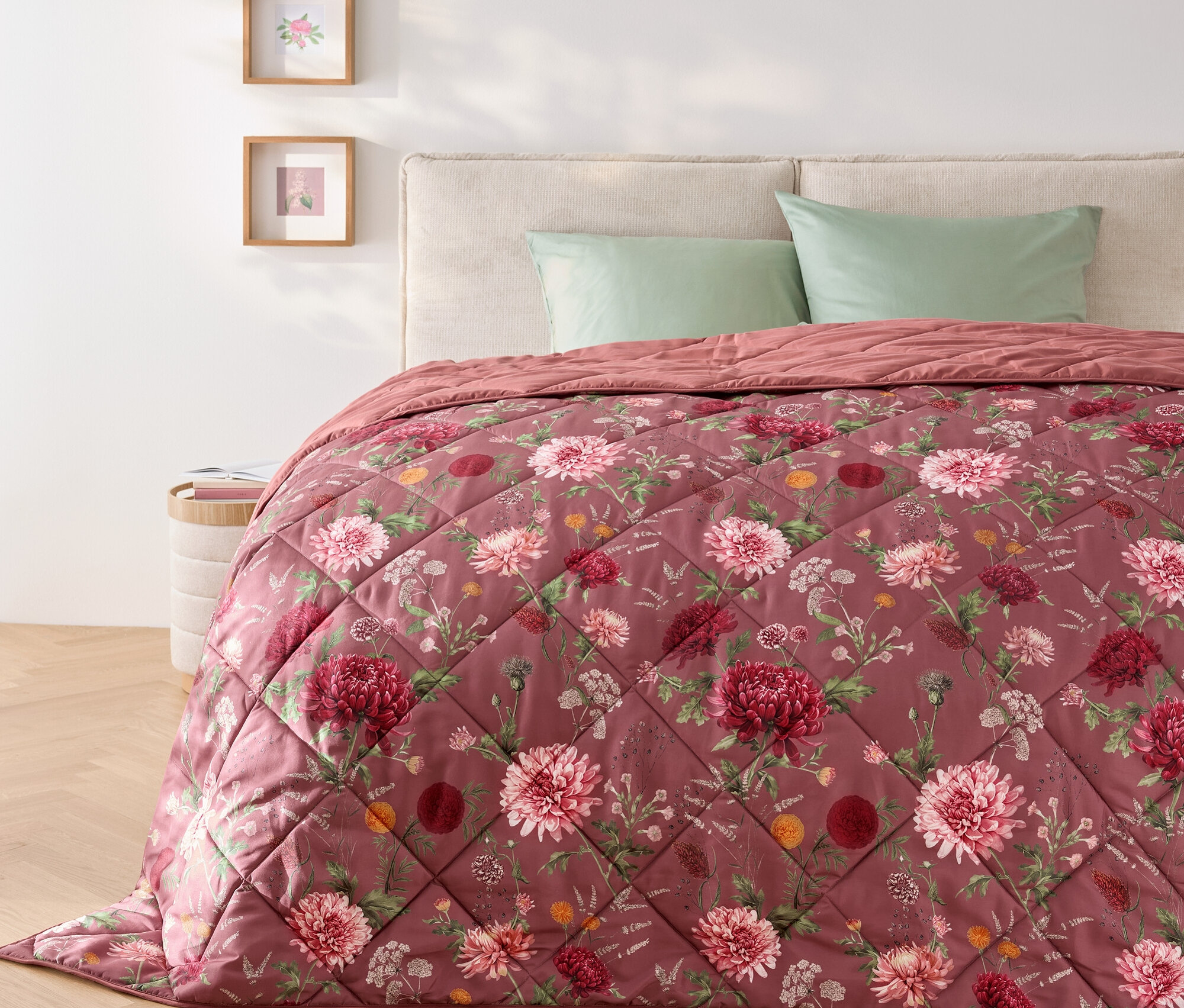 Na łóżku leży pikowana narzuta w kwiaty i dwie zielone poduszki.