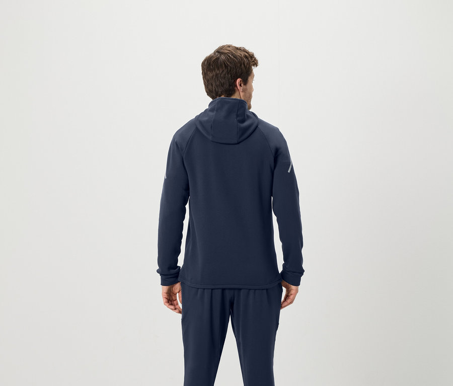 Mężczyzna tyłem do kamery ma na sobie granatową bluzę z kapturem i spodnie dresowe.