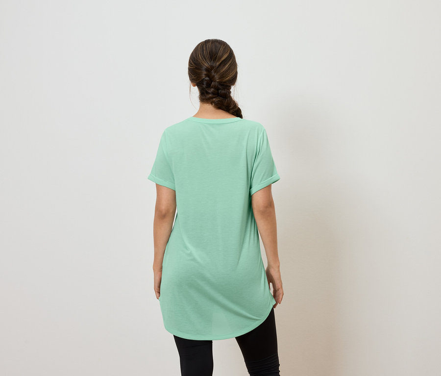 Kobieta tyłem do kamery ma na sobie zieloną koszulkę i czarne legginsy.