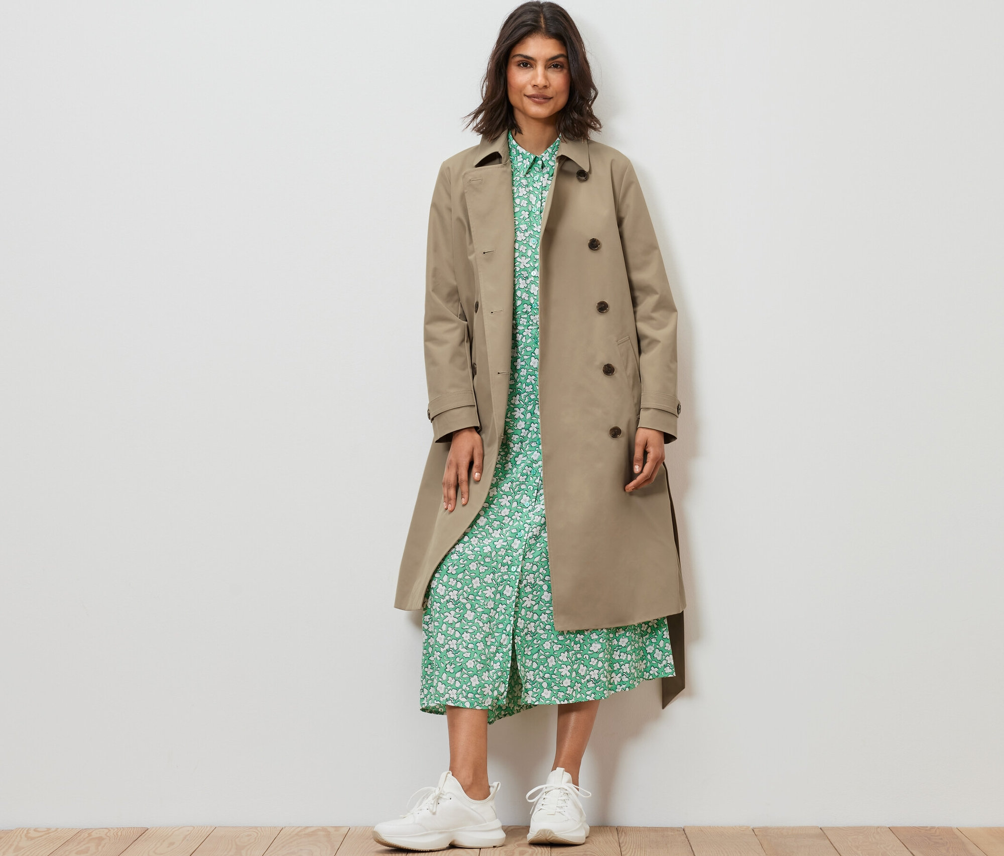 Kobieta stoi w piaskowym trenczu.