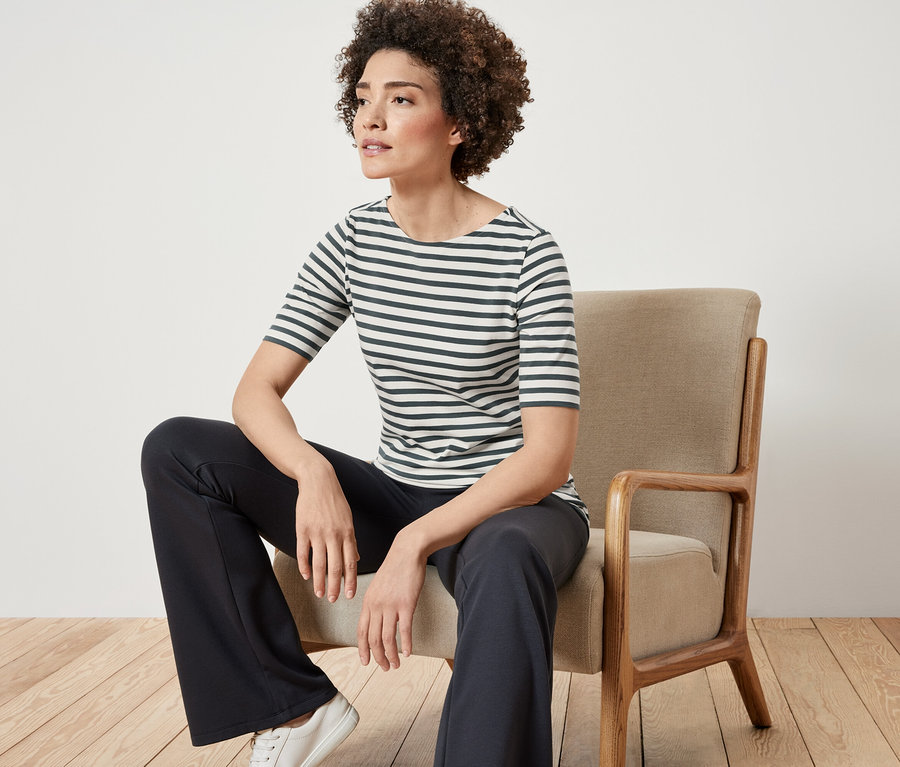 Kobieta siedzi na krześle i ma na sobie zieloną koszulkę w paski z półdługim rękawem.