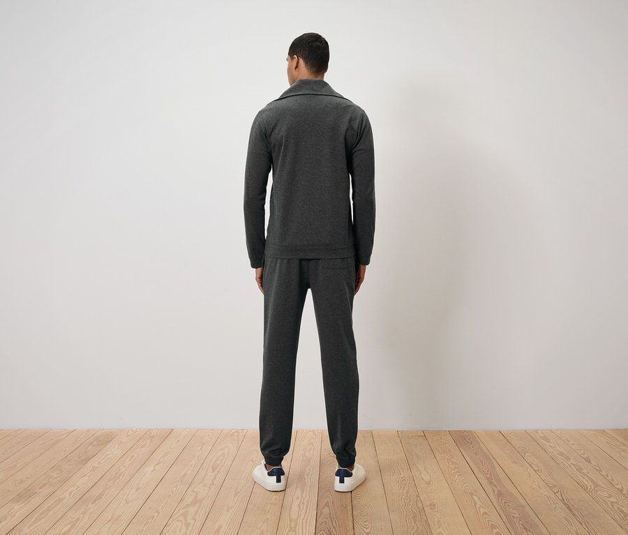 Mężczyzna tyłem do kamery ubrany w ciemnoszary dres i białe tenisówki.