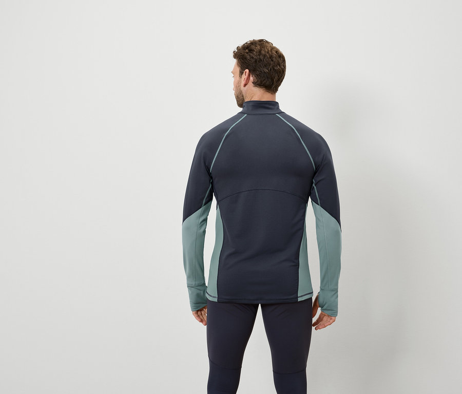Mężczyzna tyłem do aparatu ma na sobie granatową bluzę z długim rękawem z szarozielonymi panelami i granatowe legginsy.