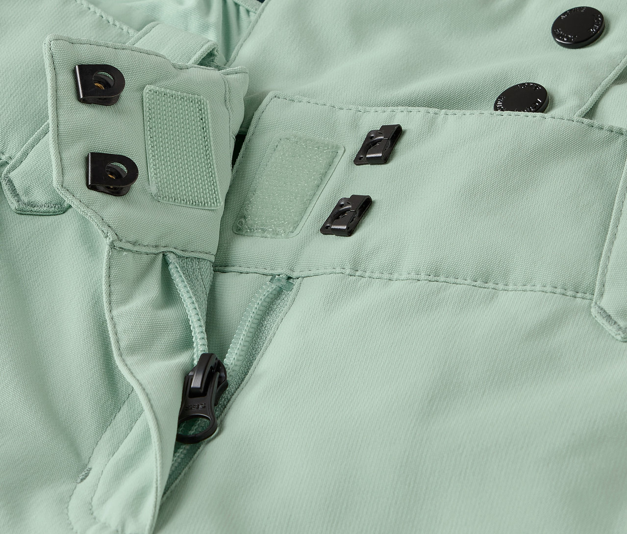 Szczegół jasnych, zielonych spodni z zamkiem błyskawicznym i zapięciem na guziki.