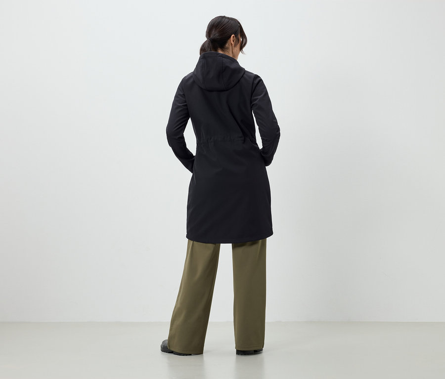 Kobieta tyłem do kamery ma na sobie czarny płaszcz i zielone spodnie.