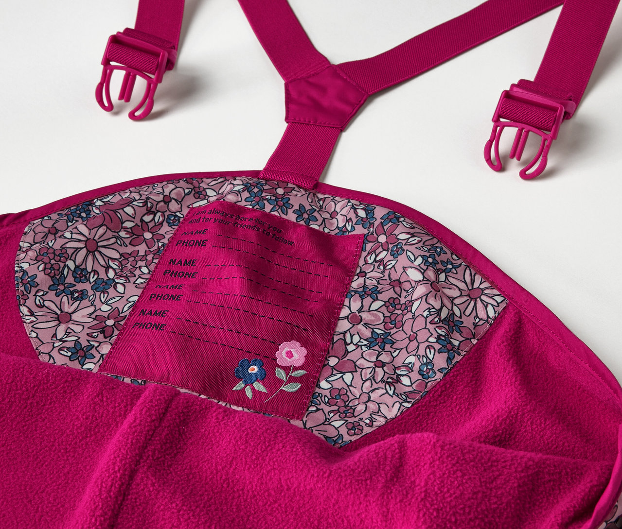 Szczegół termoaktywnych spodni przeciwdeszczowych w kwiaty dla dzieci, w tym detale takie jak szelki i metka na imię.