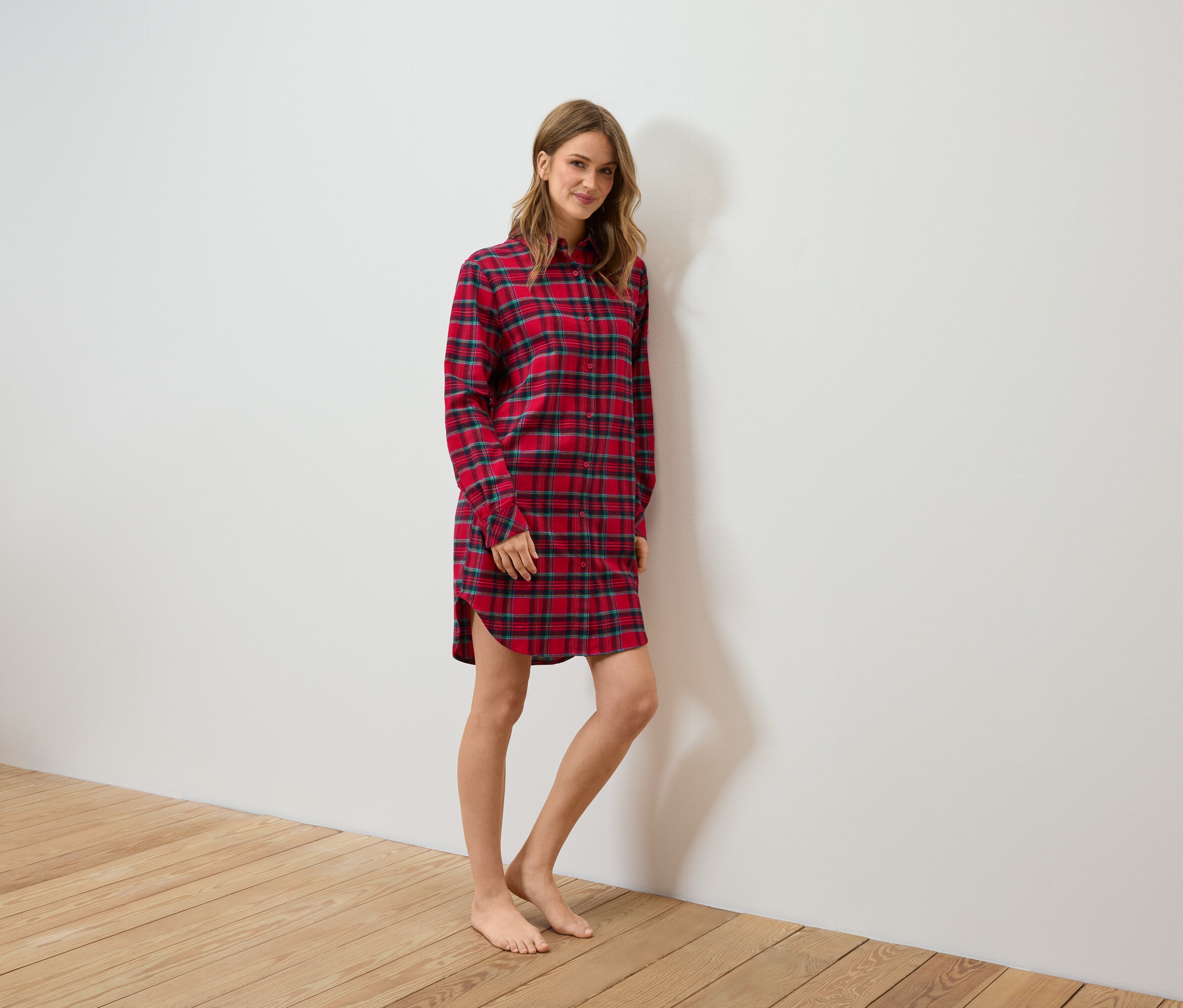 Kobieta stoi, ubrana w czerwoną, flanelową koszulę nocną w kratę.