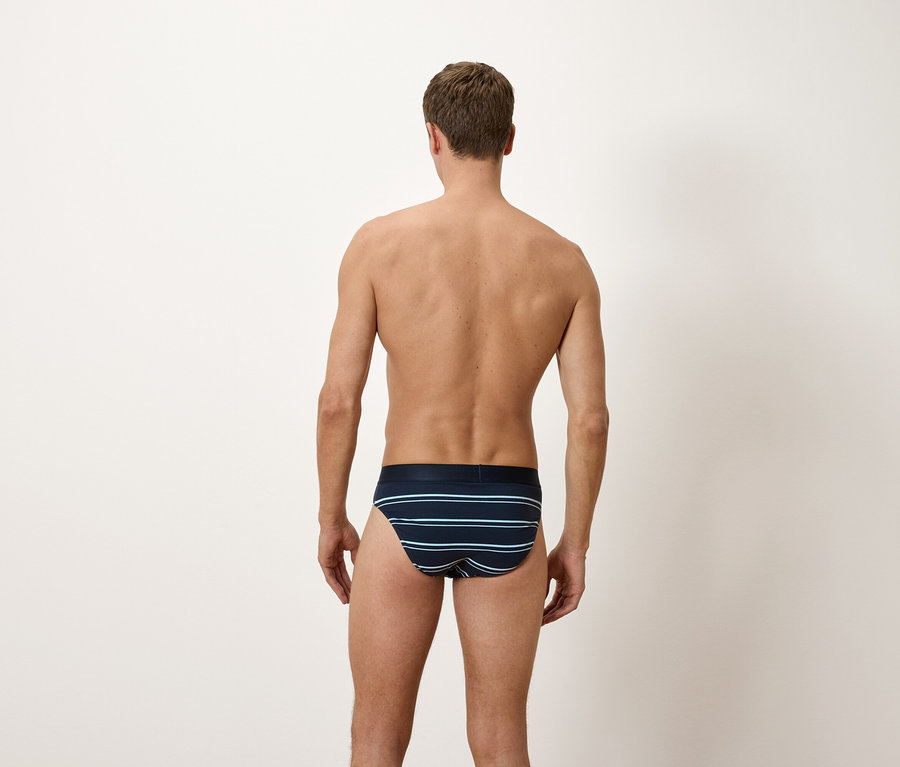 Mężczyzna tyłem do aparatu, ubrany w niebieskie slipy w poziome paski.