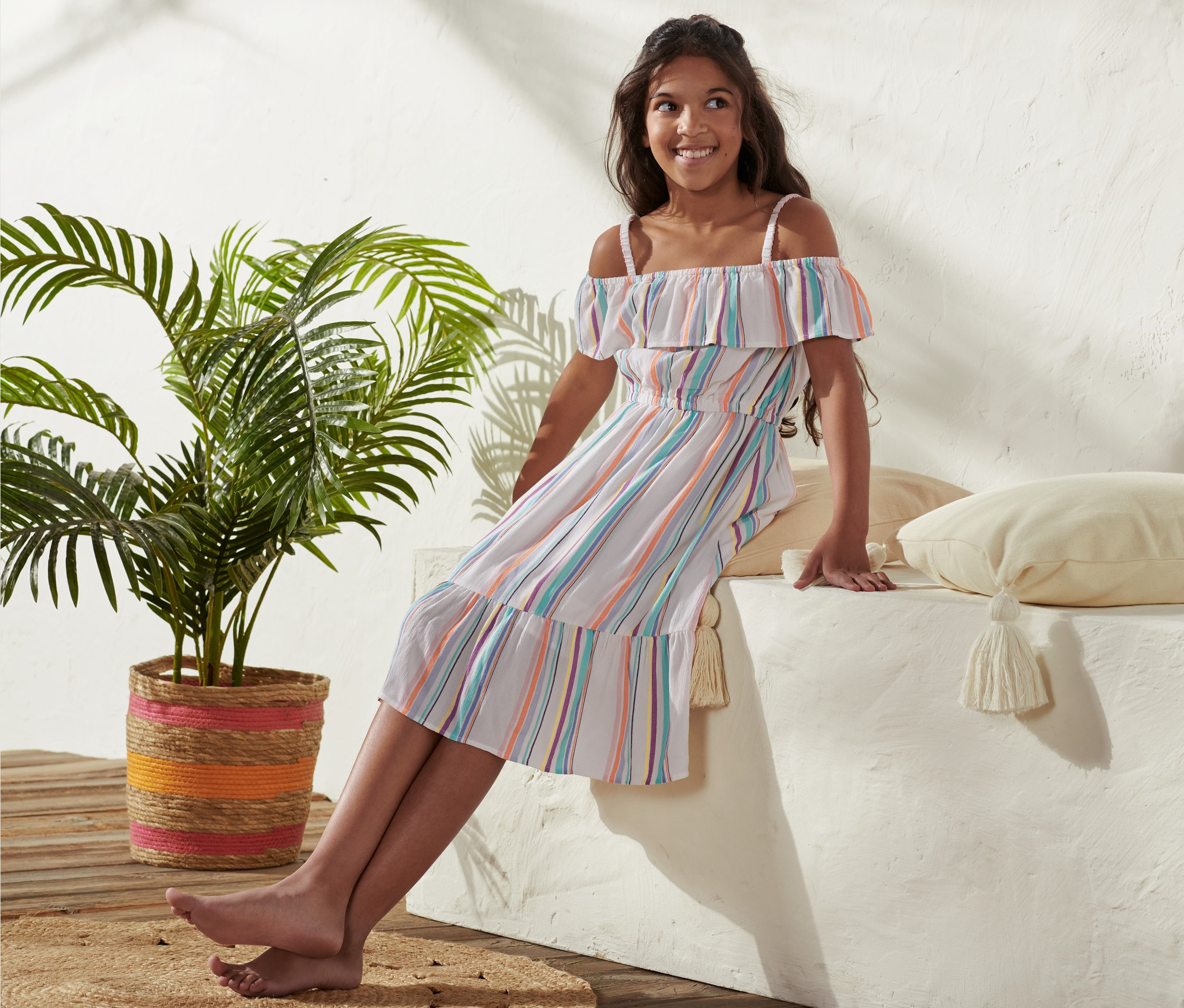 Dziewczyna siedzi na murku, ubrana w tkaną sukienkę z wiskozy.