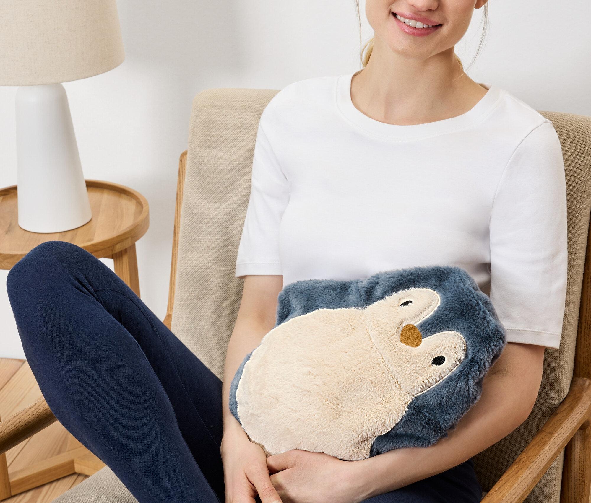 Kobieta siedzi w fotelu i trzyma pluszowy termofor pingwina.