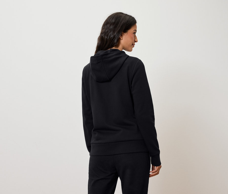 Kobieta z tyłu ma na sobie czarną bluzę z kapturem i czarne spodnie.