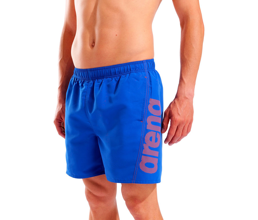Mężczyzna ma na sobie niebieskie szorty kąpielowe z logo Arena na nogawce.