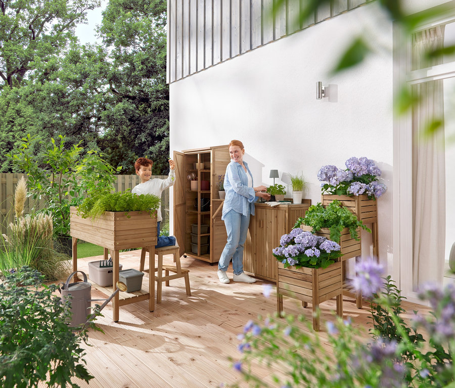 Chłopiec i kobieta pracują na drewnianym tarasie z meblami ogrodowymi i roślinami.