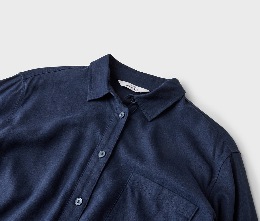 Zbliżenie granatowej koszuli z kołnierzykiem, guzikami i jedną kieszenią na piersi na neutralnym tle.