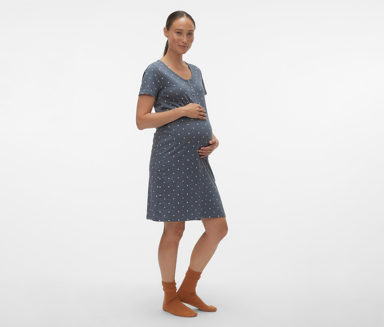 Kobieta w ciąży trzyma się za brzuch, ubrana w niebieską koszulę nocną MAMALICIOUS „MLMIRA” w białe kropki.