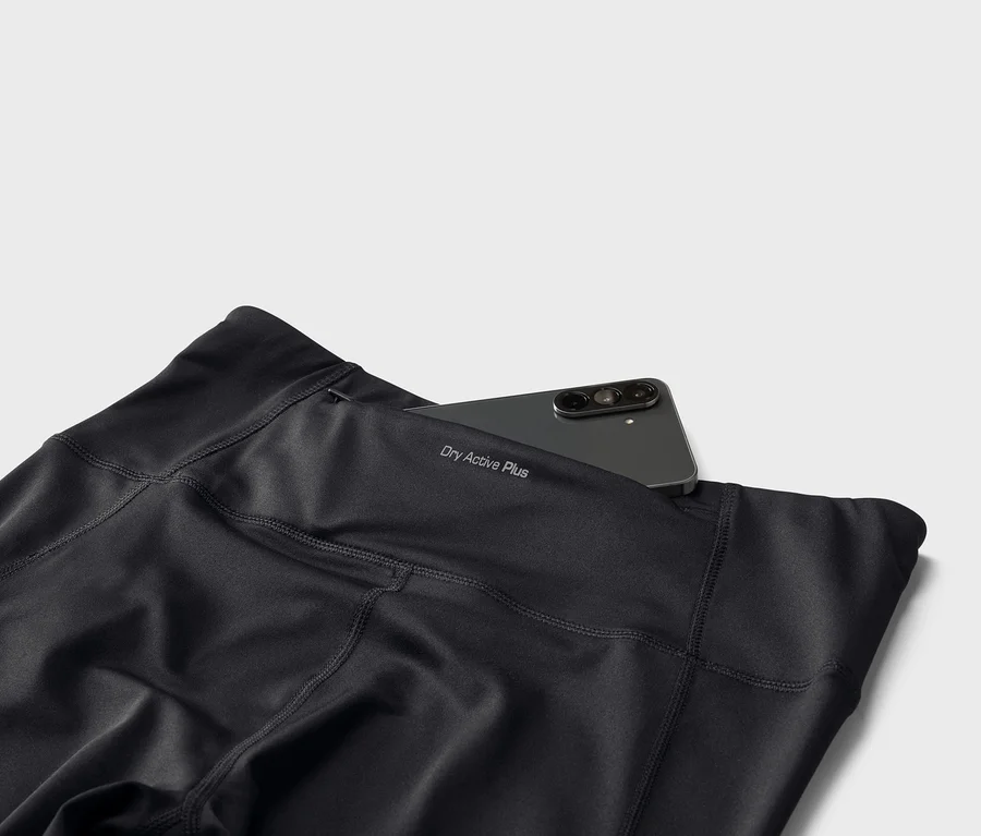 Czarne legginsy z napisem „Dry Active Plus” i smartfonem w tylnej kieszeni.