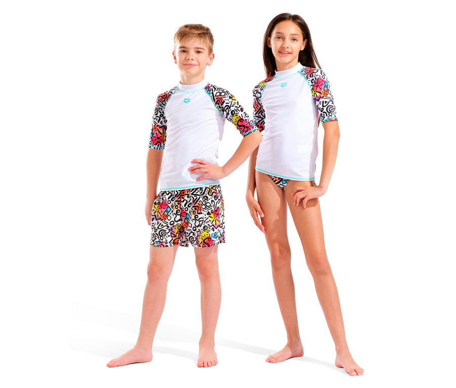 Dwoje dzieci, chłopiec i dziewczynka, stoi obok siebie na białym tle. Oboje mają na sobie białe topy z kolorowymi rękawami i kolorowe doły.